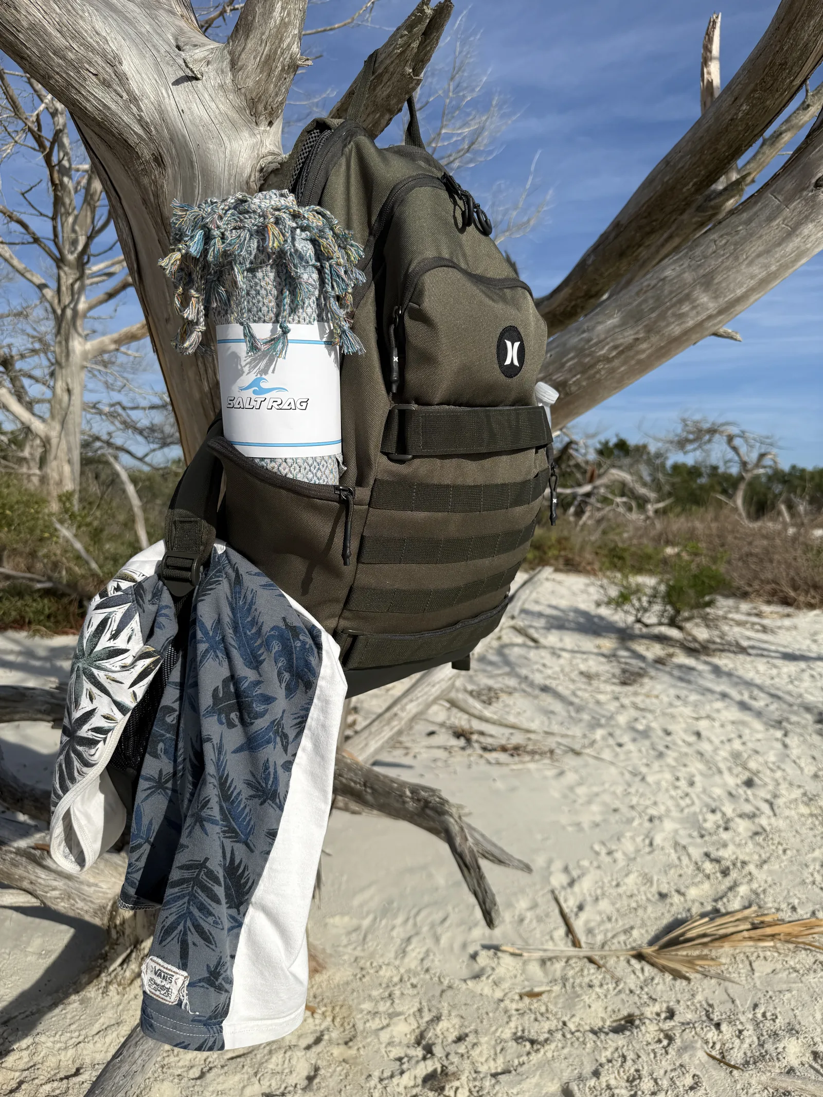A patterned Salt Rag packed in the outside pocket of a backpack beside outdoor chairs.