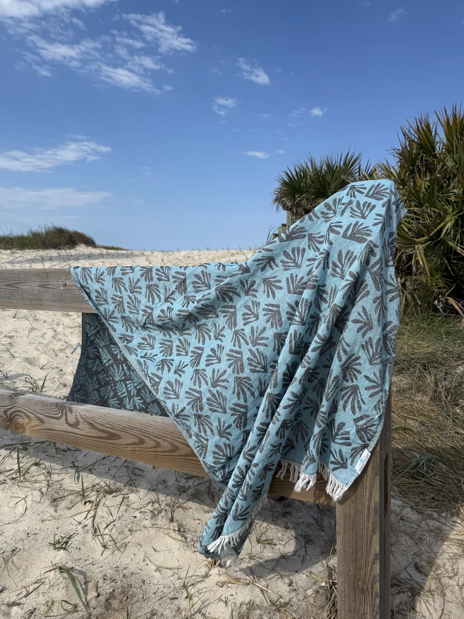 Blue leaf-patterned Salt Rag draped along a wooden beach-access rail.