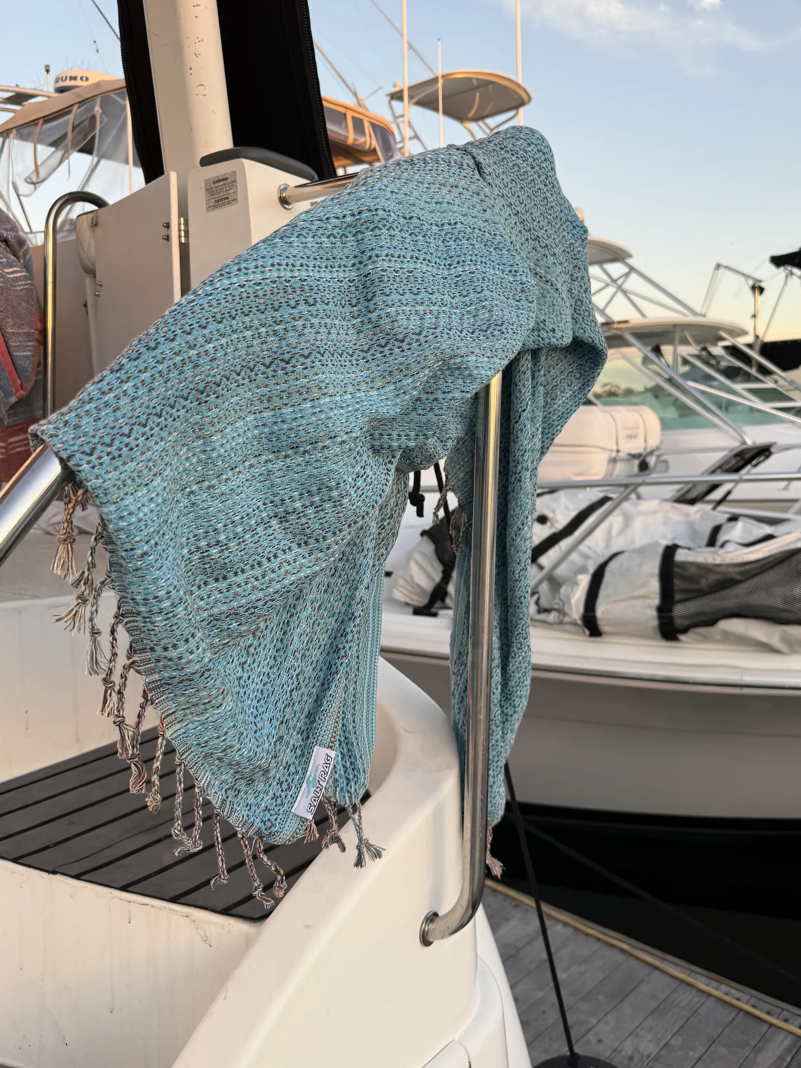 Blue woven Salt Rag draped over a boat rail, with marina boats behind it.