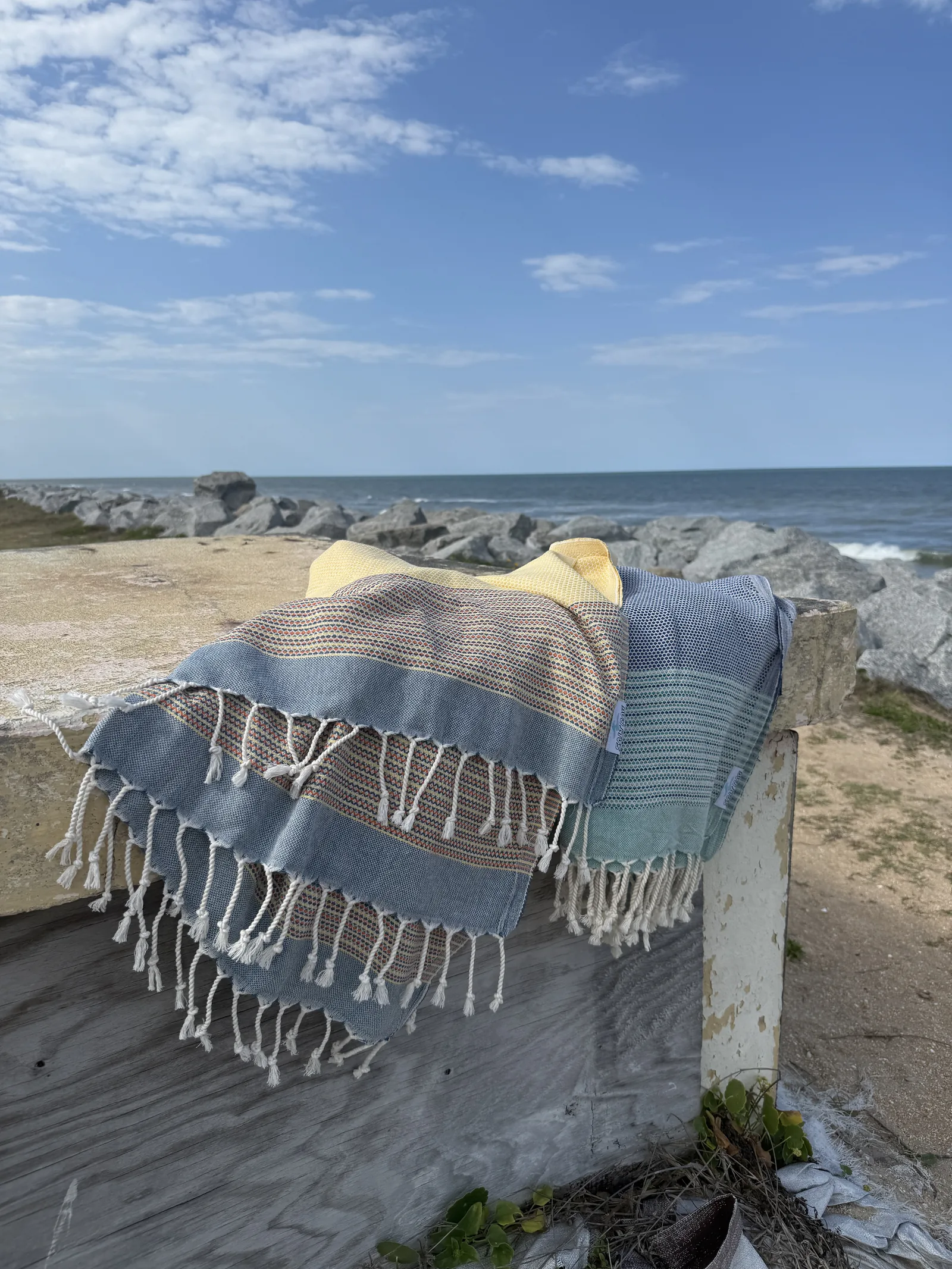 Folded Salt Rags stacked on a wooden beach-access rail with the ocean behind.