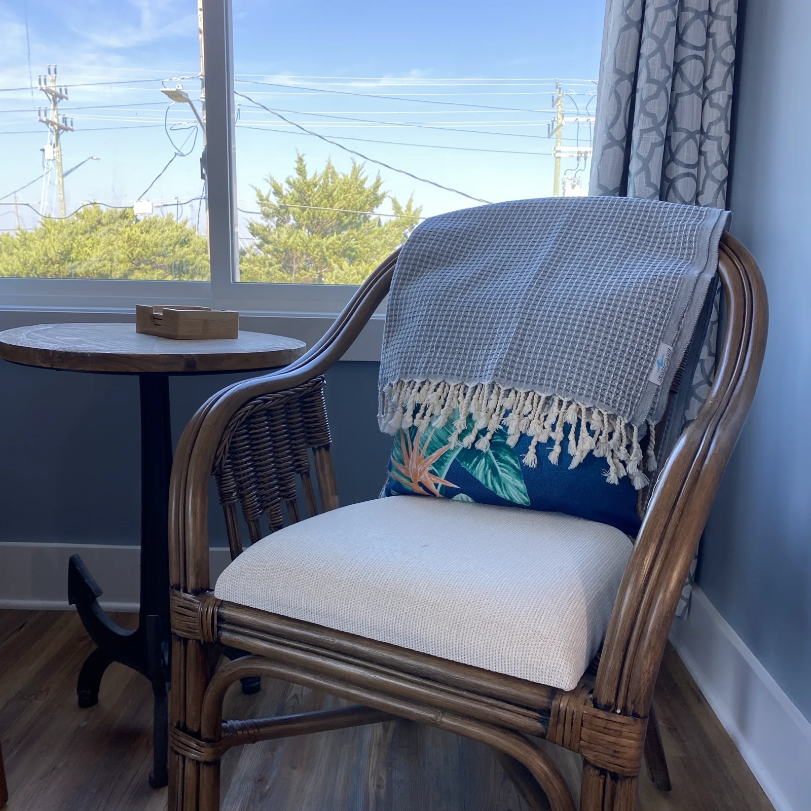 Gray patterned Salt Rag with cream fringe draped over a rattan chair beside a window.