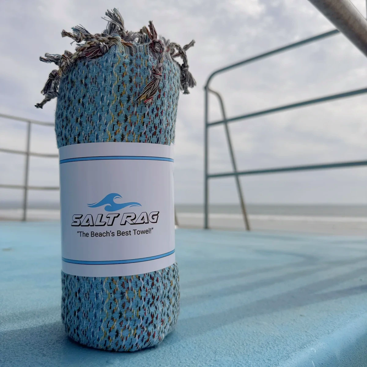 A rolled blue Salt Rag standing on a boat deck beside the water.