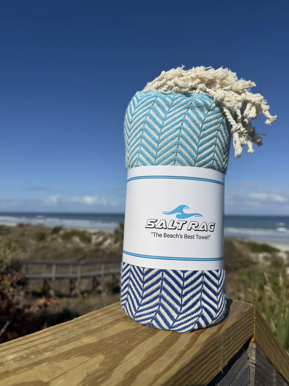 Blue-and-white rolled Salt Rag with full fringe on a coastal deck.