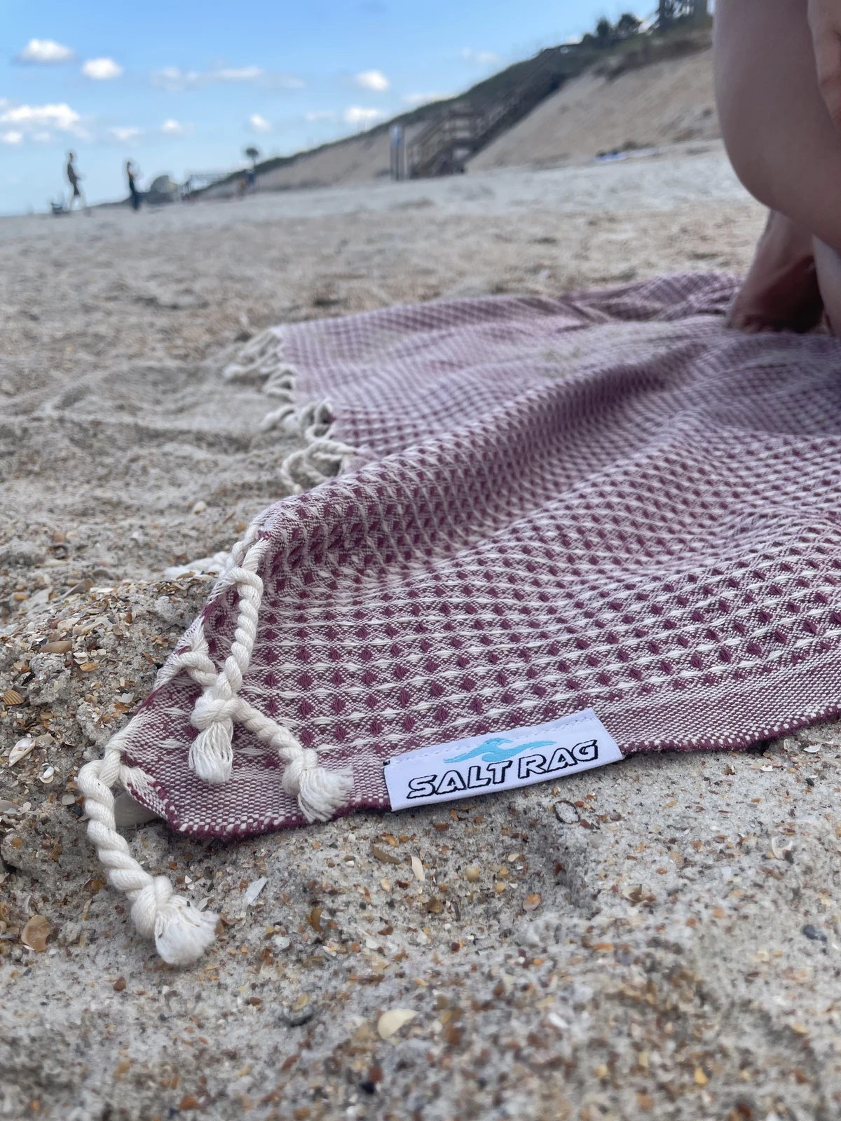 Pink cotton weave, Salt Rag label and knotted fringe against beach sand.