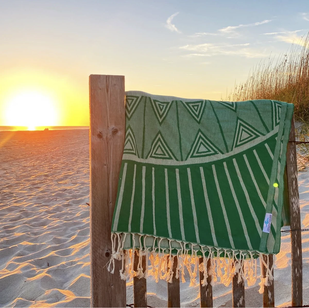 A green Salt Rag hanging on a beach fence in low sunlight.