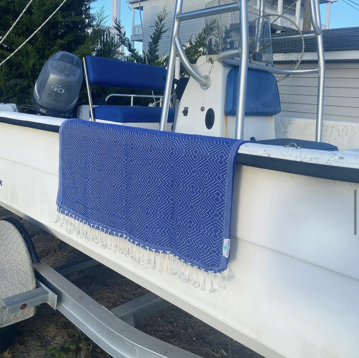 A blue geometric Salt Rag draped over the side of a boat, with cream fringe hanging free.