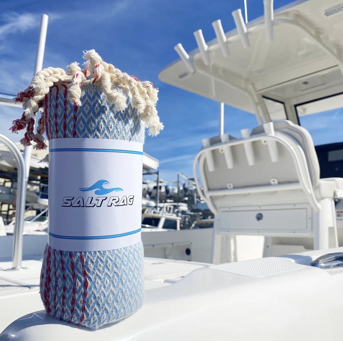 A blue and red Salt Rag rolled on a white boat deck with its label and fringe visible.