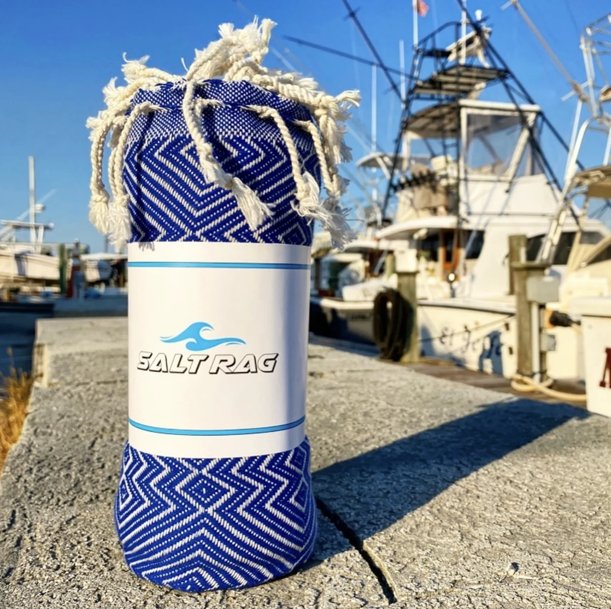 A blue patterned Salt Rag rolled on a dock beside fishing boats.