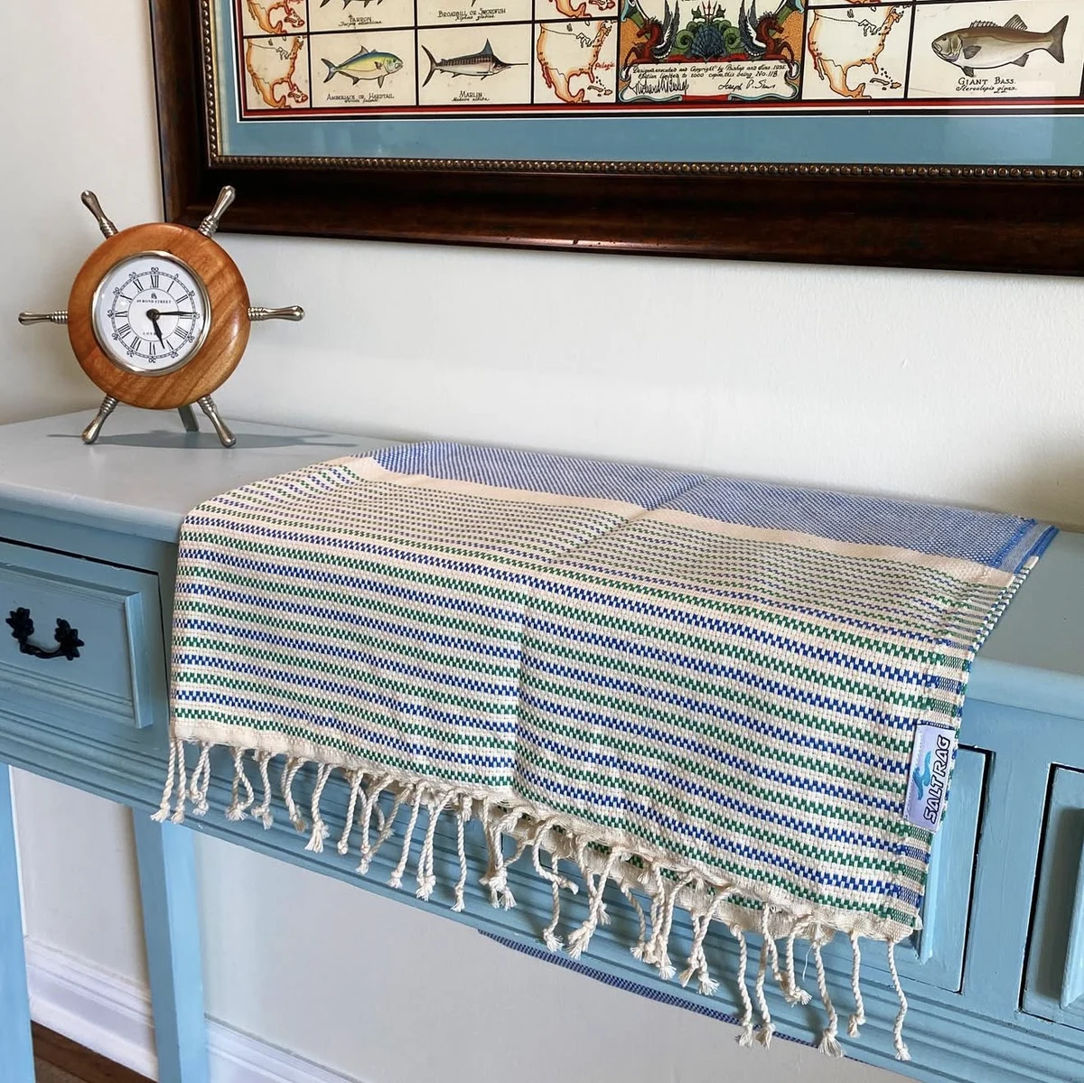 A striped Salt Rag draped over a blue console table beneath nautical artwork.