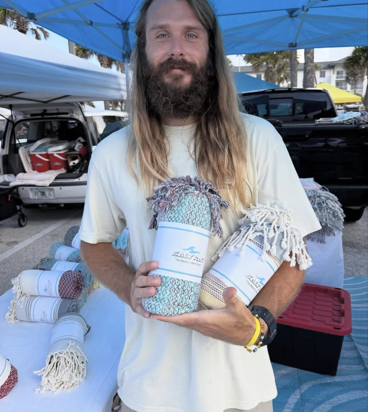 A vendor holding two rolled Rags under the blue market canopy.