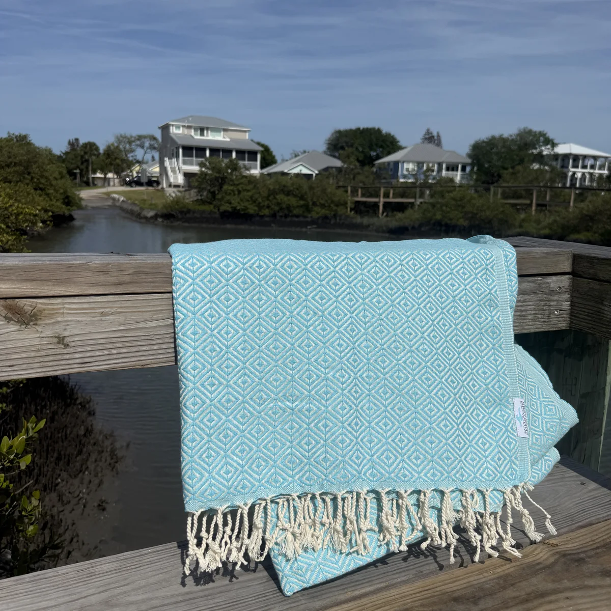 Pale blue woven Salt Rag hanging over a waterfront rail, with its fringe visible.