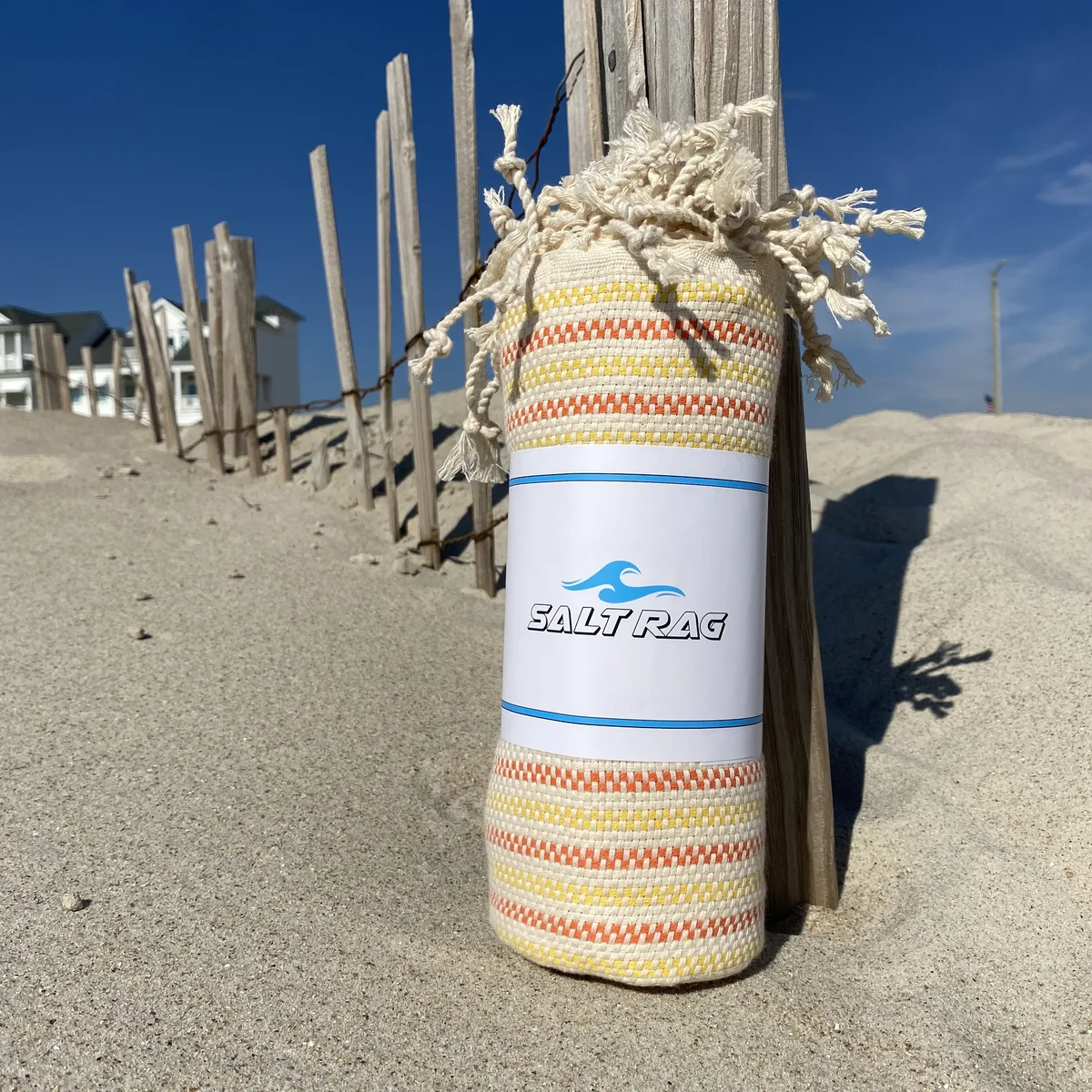 Yellow and rose striped Salt Rag rolled beside beach-access fencing.