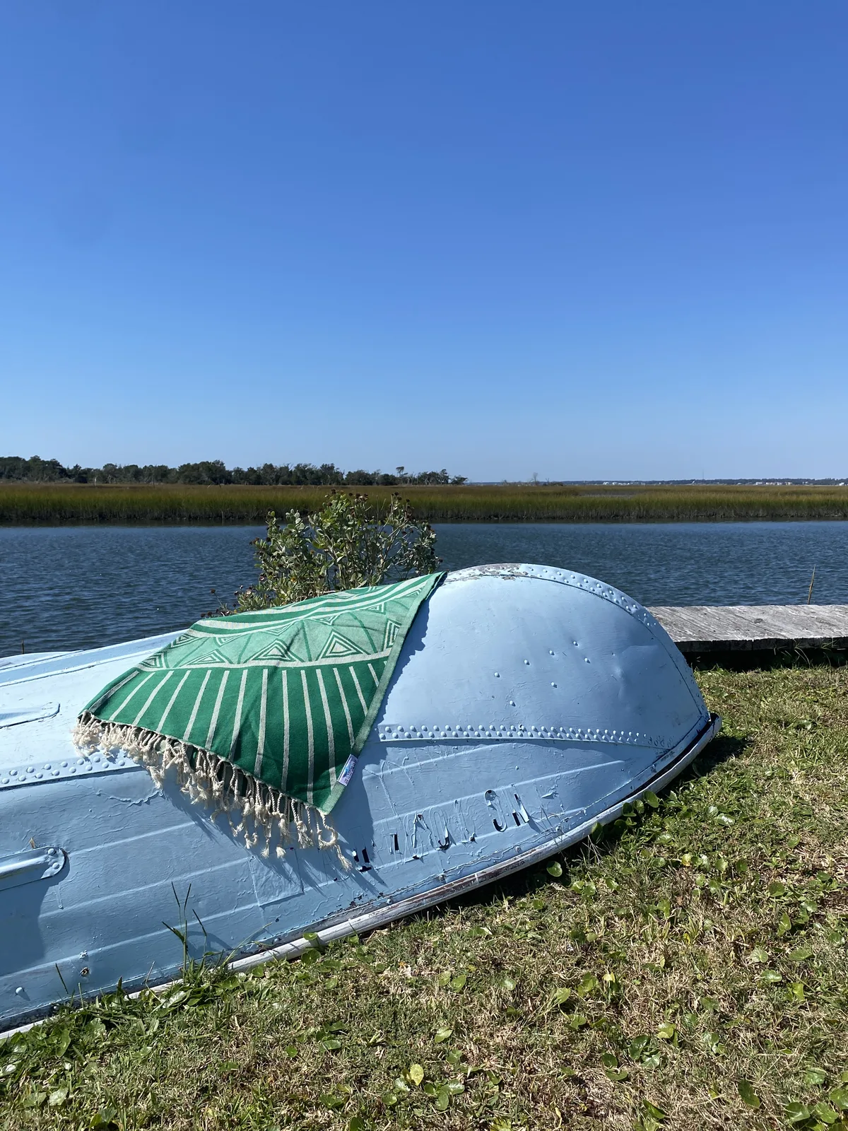 Green striped Salt Rag draped over a small overturned boat beside the water.