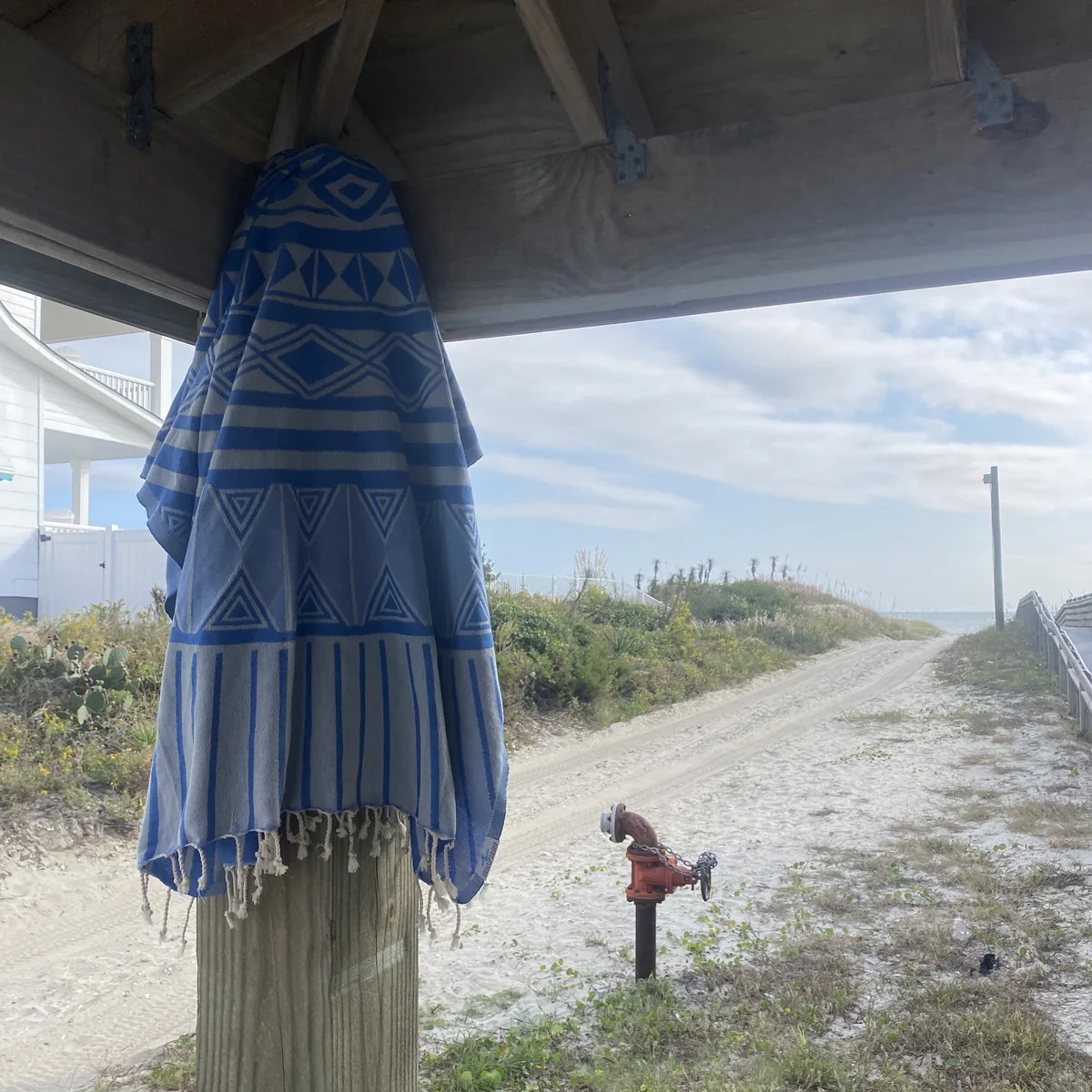 Blue striped Salt Rag hanging beneath a beach-access shelter.