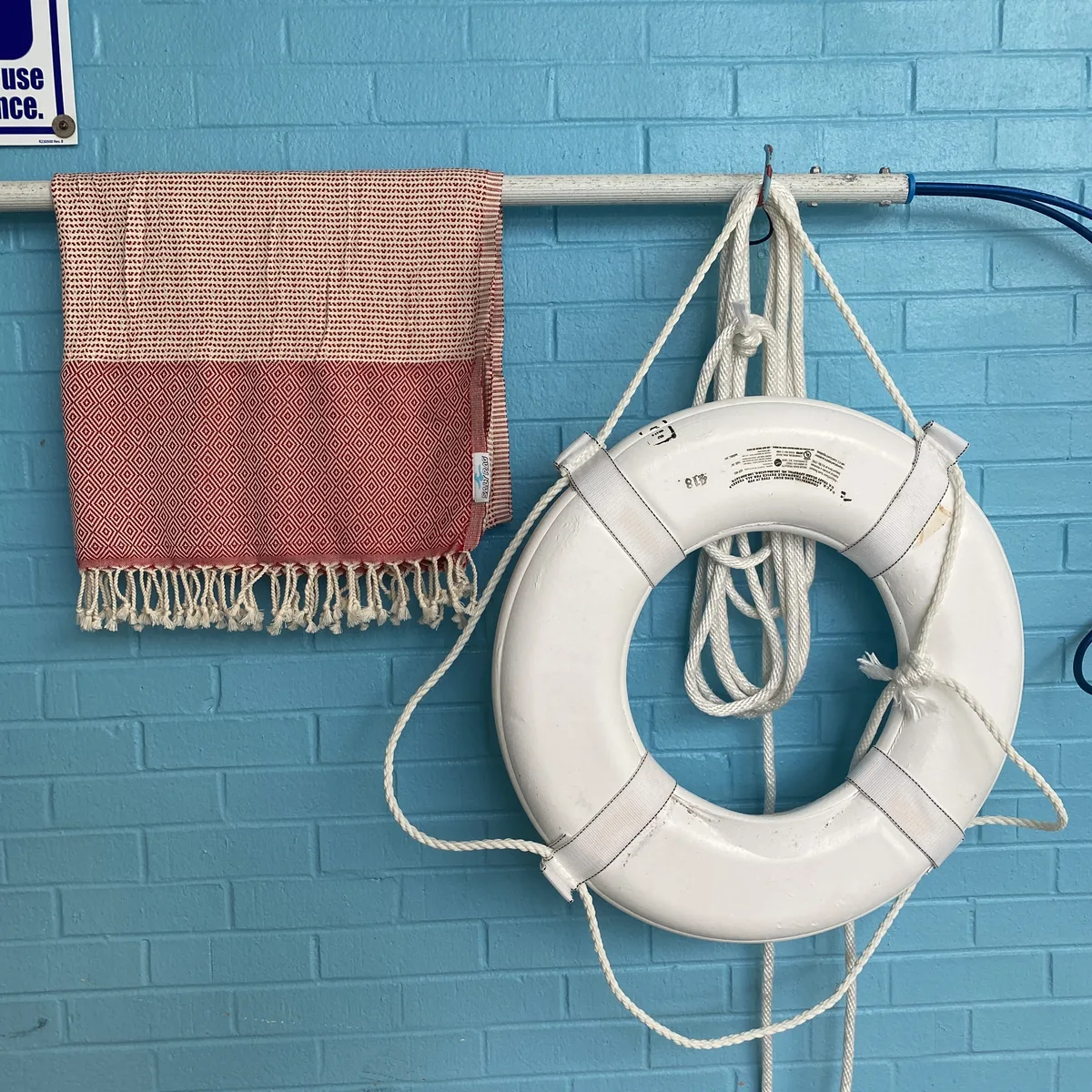 Rose woven Salt Rag hanging beside a life ring on a blue wall.