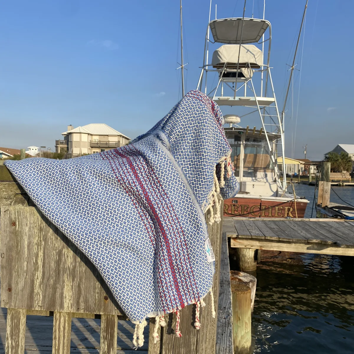 Blue and rose striped Salt Rag hanging over a wooden dock rail.