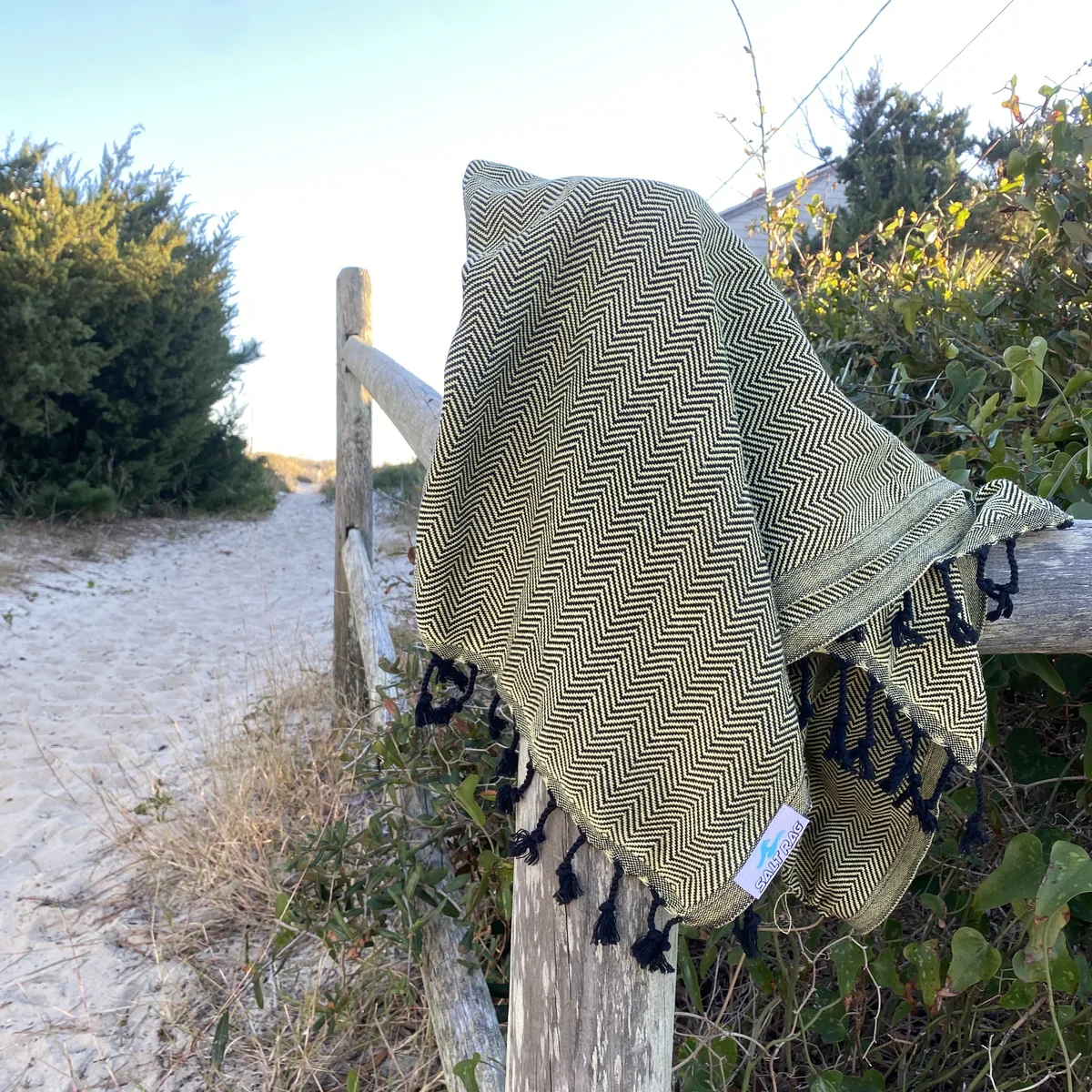 Olive Salt Rag draped over a weathered fence with its woven cotton and fringe visible.