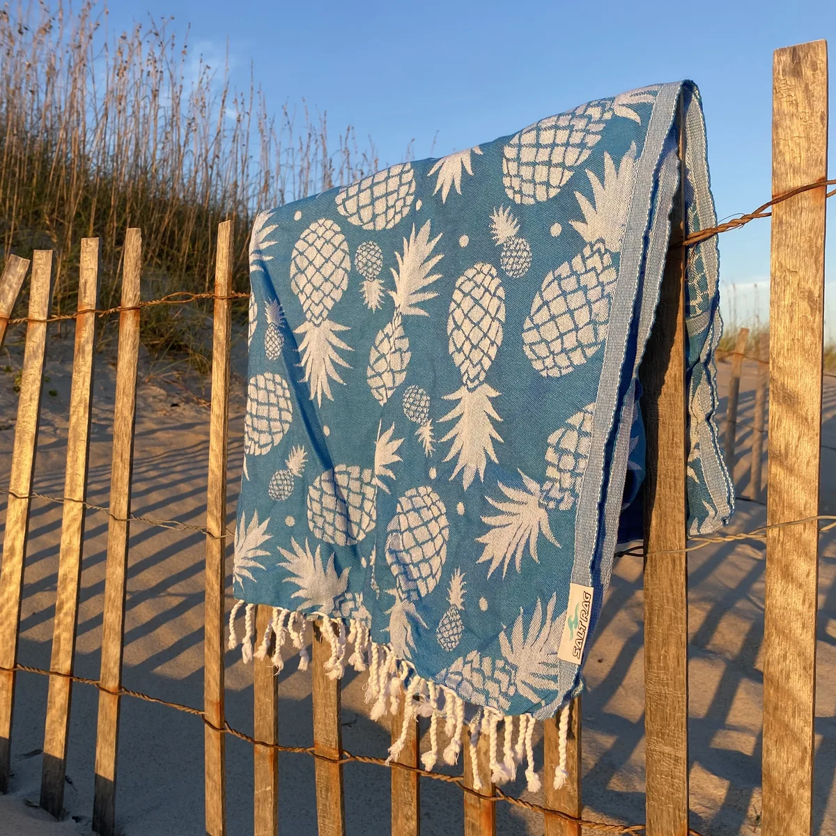 Blue pineapple-patterned Salt Rag draped over a beach fence.