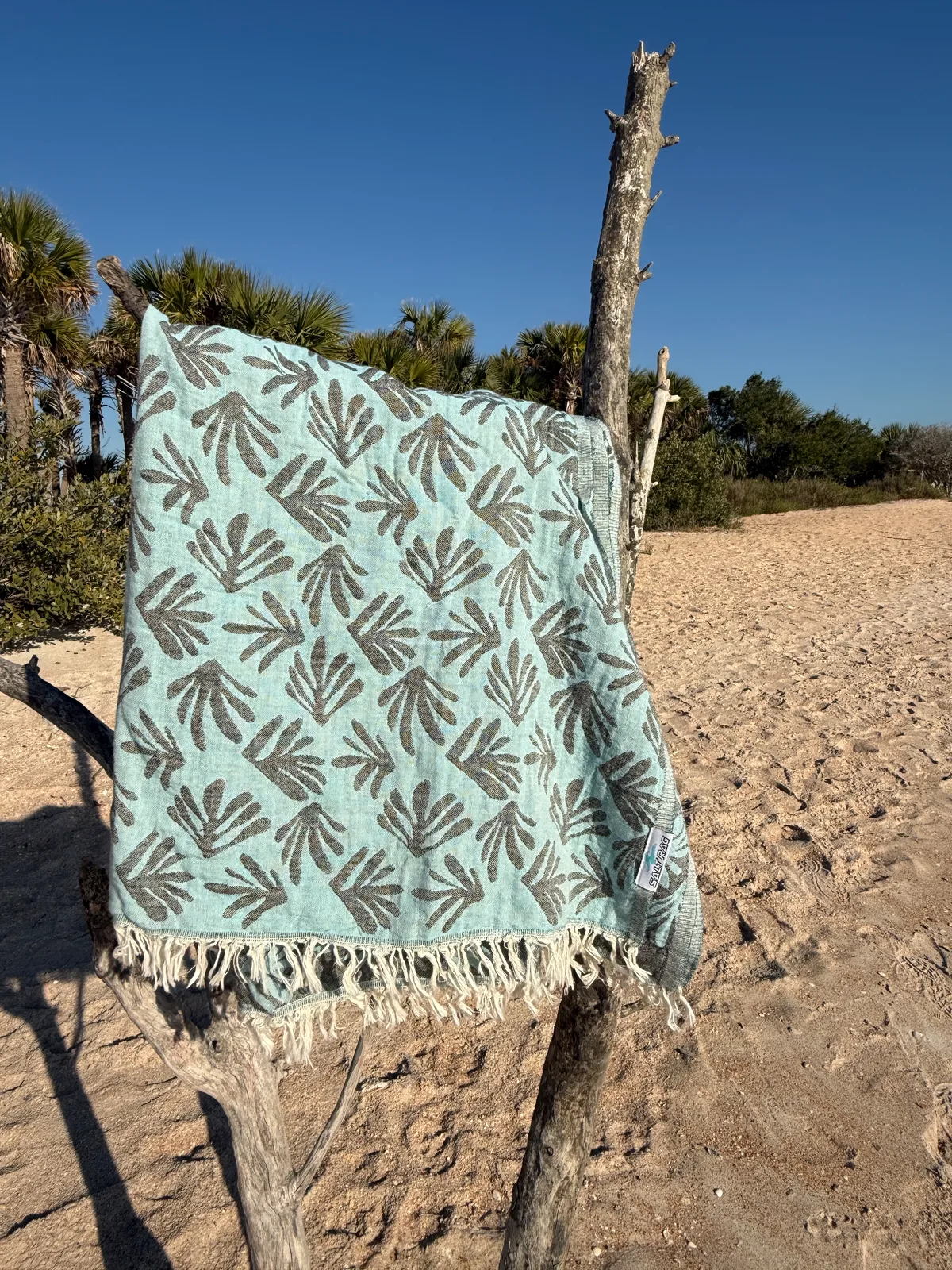 Green leaf-patterned Salt Rag spread open over driftwood on the beach.