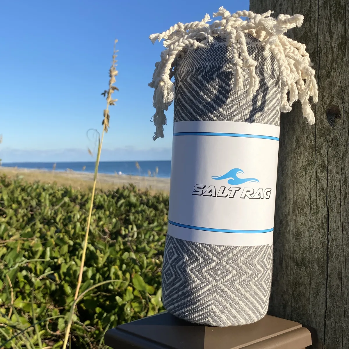 A rolled blue Salt Rag with its paper band and fringed end visible on a wooden rail.