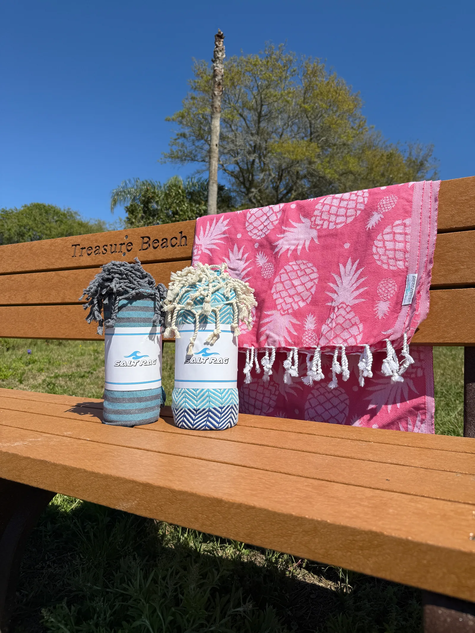 Pink leaf-patterned Salt Rag draped over a beach-access bench beside two rolled Rags.