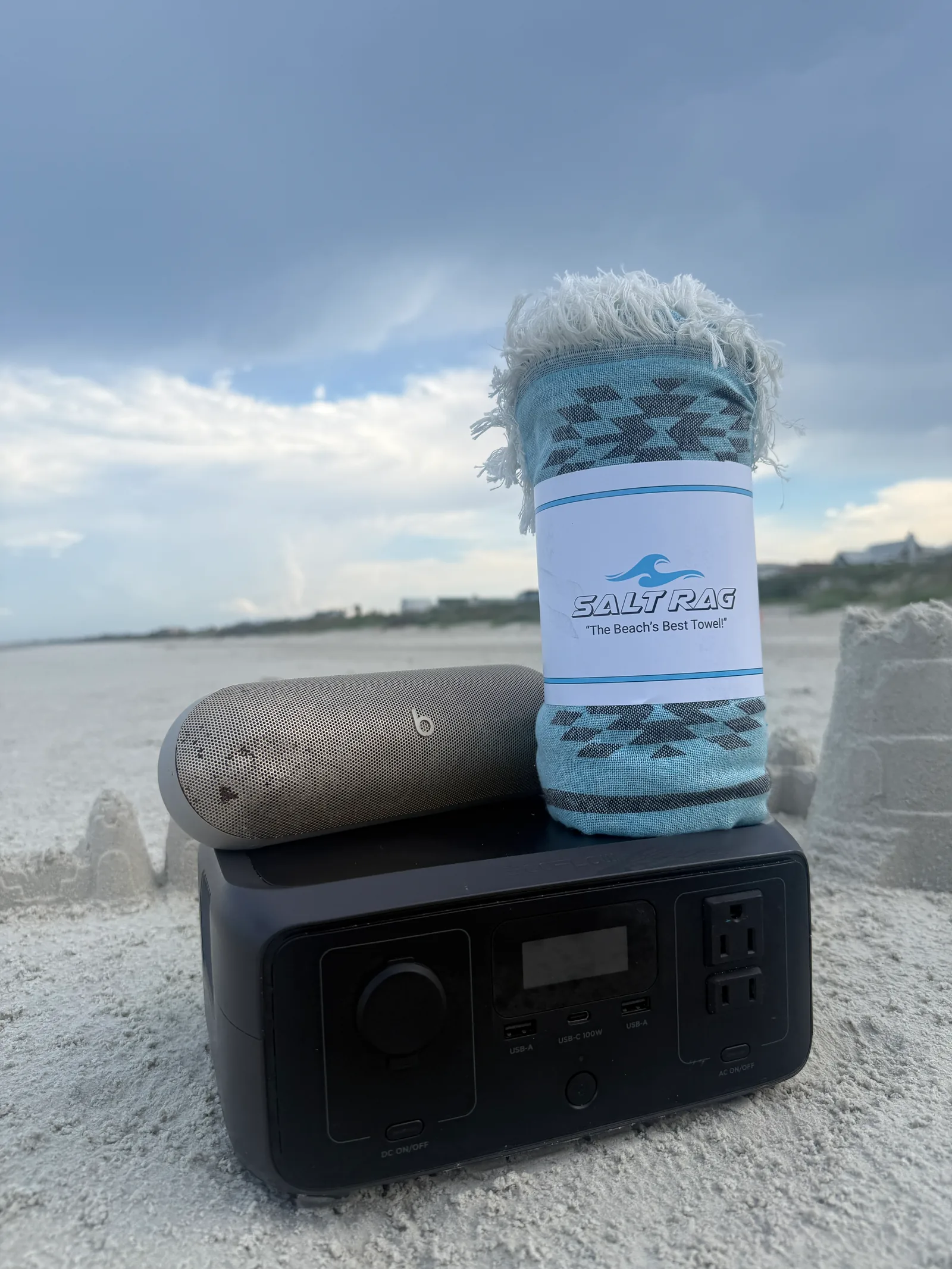 Rolled pale blue patterned Salt Rag beside beach gear on the sand.