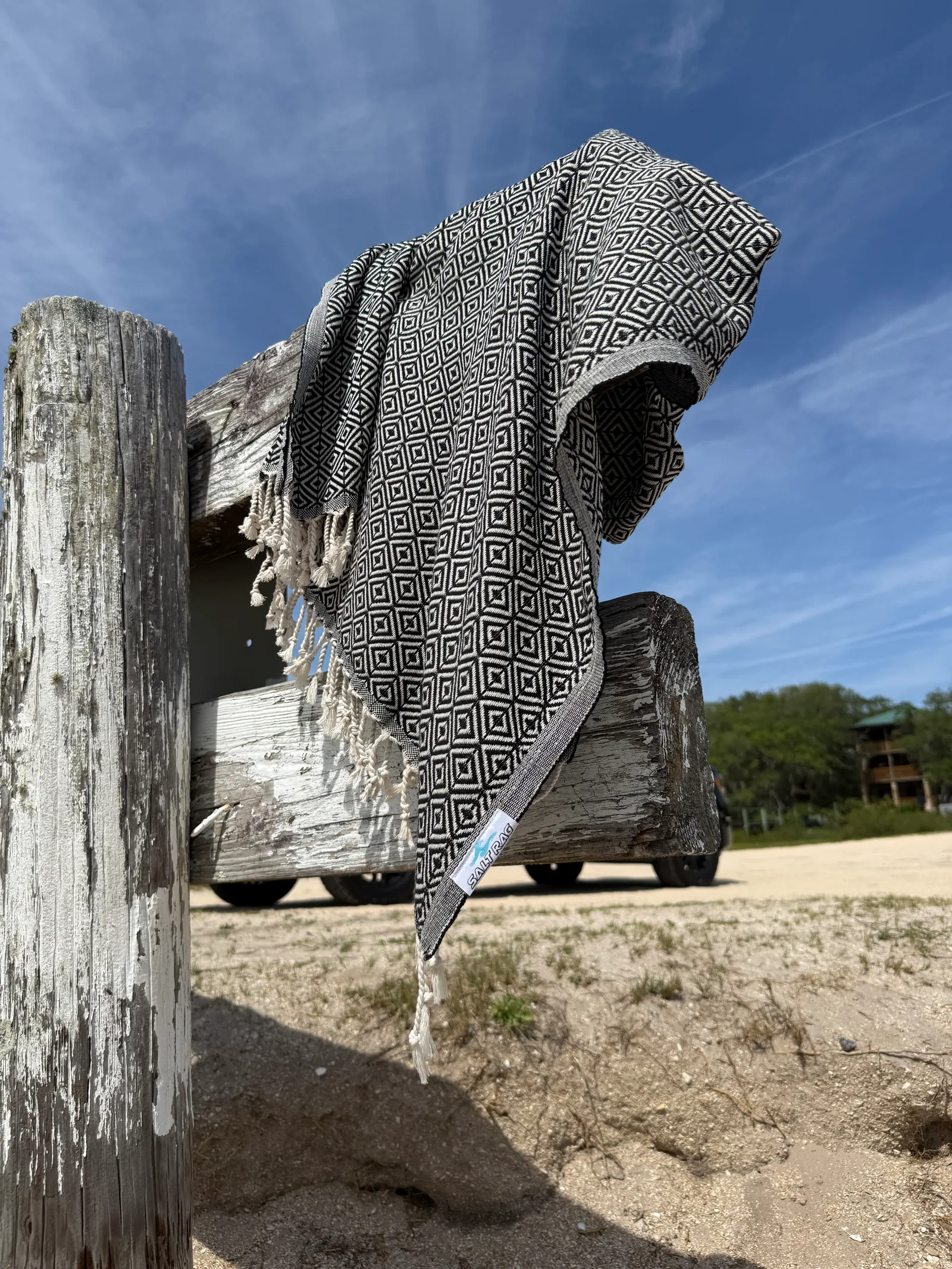 Charcoal geometric-patterned Salt Rag hanging over a weathered wooden fence with fringe visible.
