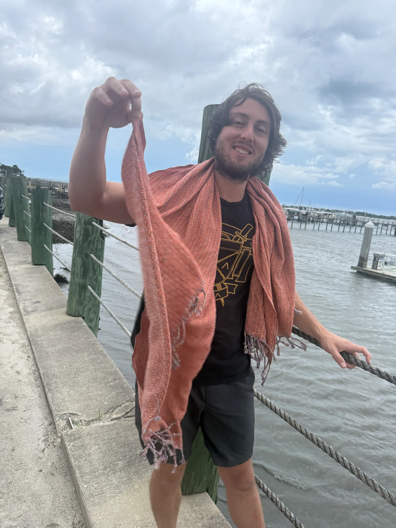 A peach Salt Rag draped over a person's shoulders beside the waterfront.