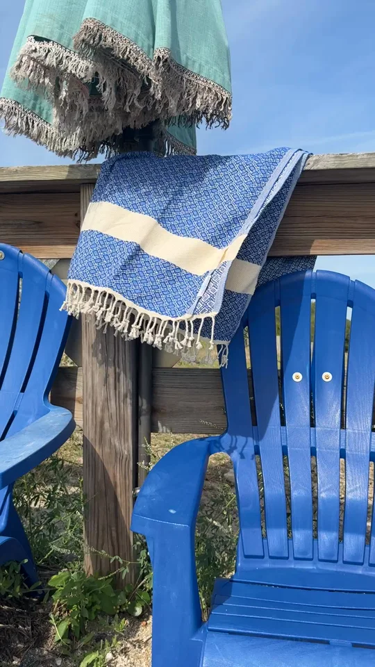 A navy and cream Salt Rag hanging from a waterfront rail beside blue chairs.