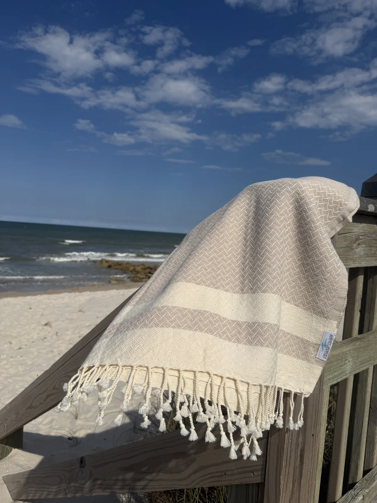 White Salt Rag with blue stripes and full fringe on a beach railing.