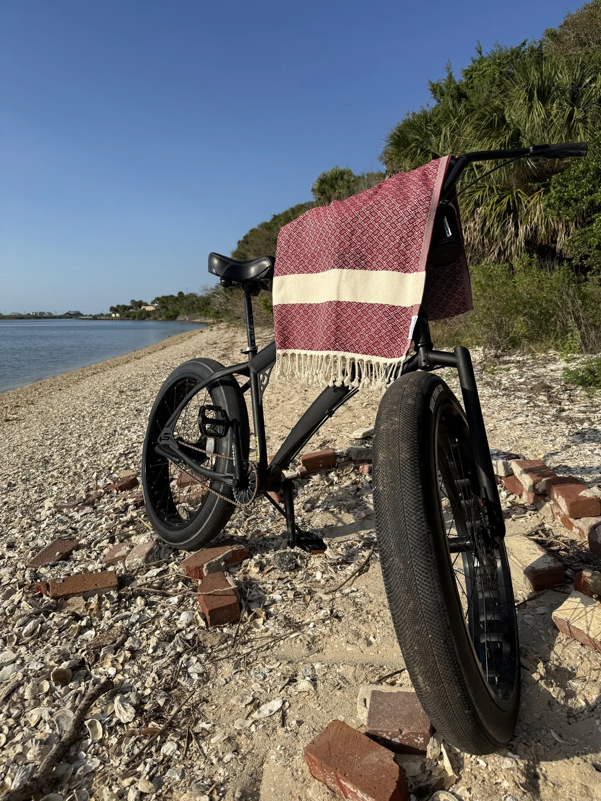 Red-pattern Rag draped on fat-tire bike at shell shoreline.